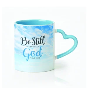 Ceramic coffee mug with a heart-shaped handle featuring the scripture Psalm 46:10, Be still and know that I am God, displayed in elegant typography on a religious gift mug.