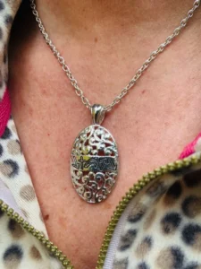 A close-up of a delicate oval pendant from the Witness jewellery collection for women, featuring intricate symbolic engravings on a polished metal surface.