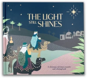 Hardcover copy of The Light Still Shines Christmas book featuring gold foil detailing on the cover and three included rub-down transfer sheets.
